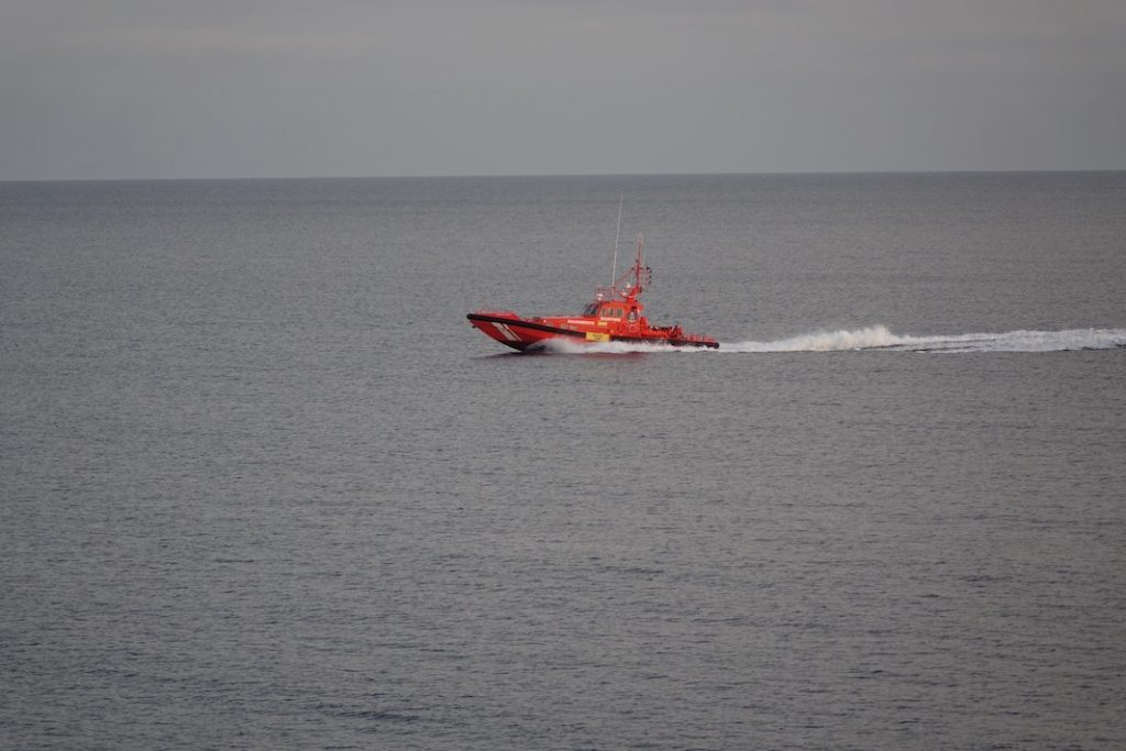 La barca de Salvament Marítim arribant al Port. A la part de darrere, els migrants, asseguts